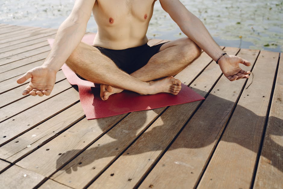 Woman performing a gentle backbend yoga pose on a wooden deck by calm water.